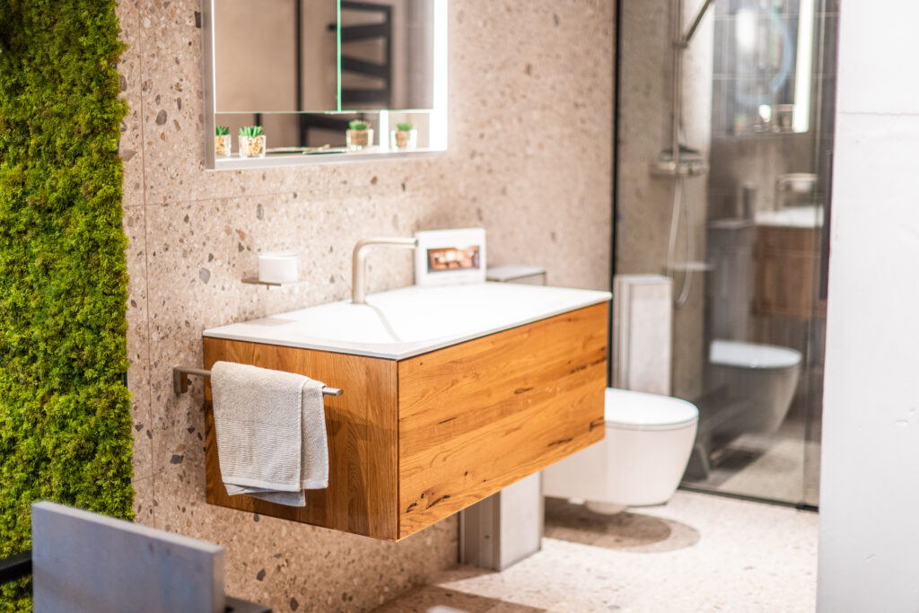 Modernes Badezimmer mit Terrazzo-Fliesen, Holzwaschtisch und Glasdusche im Schauraum von MABELA Fliesen und Handels GmbH.