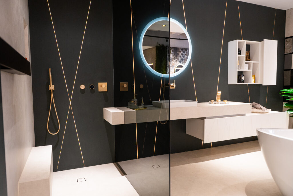 Modernes Designerbad mit LED-Spiegel, großformatigen Fliesen und goldenen Armaturen bei MABELA Fliesen und Handels GmbH – exklusive Badgestaltung im Schauraum.