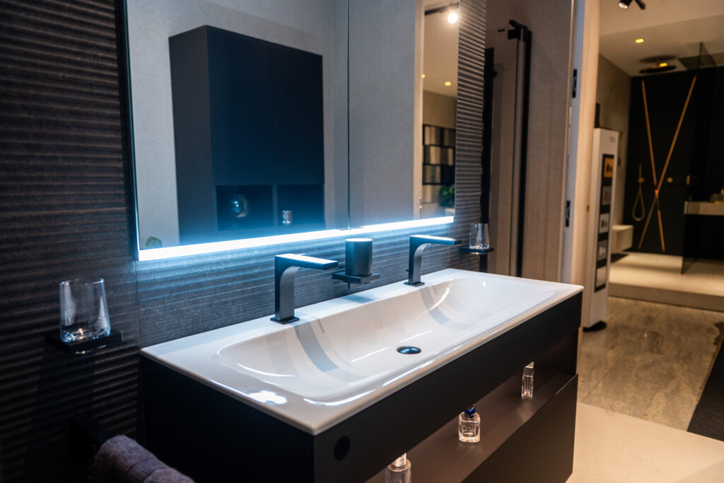 Modernes Doppelwaschbecken mit LED-Spiegel und hochwertigen Wandfliesen bei MABELA Fliesen und Handels GmbH – stilvolle Badgestaltung im Schauraum.